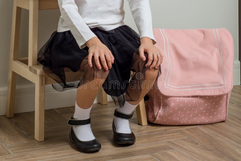 Child little girl going to school, at home with backpack sitting on chair in the hallway near the front door