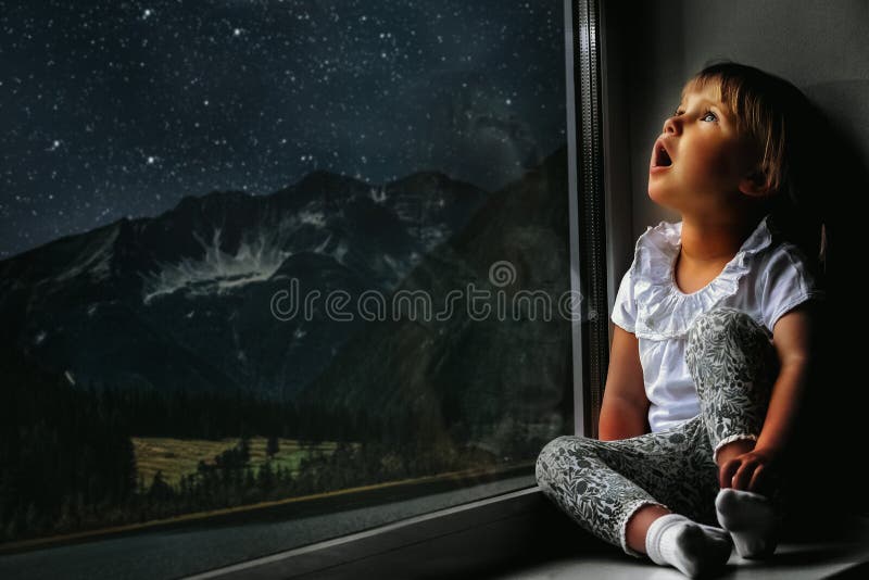 child looks out the window into the night sky