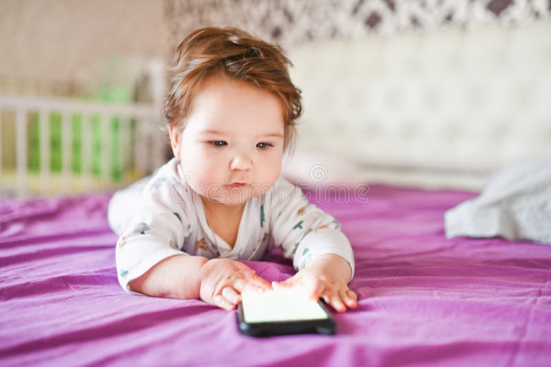 Child and Mobile Device. Little Girl in Bed Looking at a Smartphone
