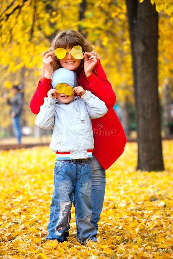 Il bambino e la madre, chiusi gli occhi con foglie di autunno.