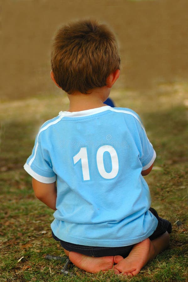 Rear view of the back of a white caucasian boy child wearing a light blue shirt with a number ten on it waiting and sitting on the lawn. Boring kid white stock images, royalty-free photos and pictures