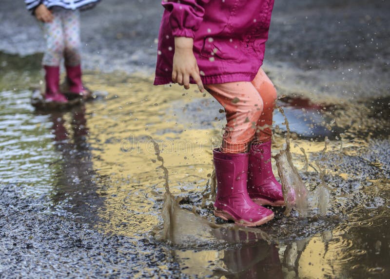 Playful child outdoor jump into puddle in boot after rain