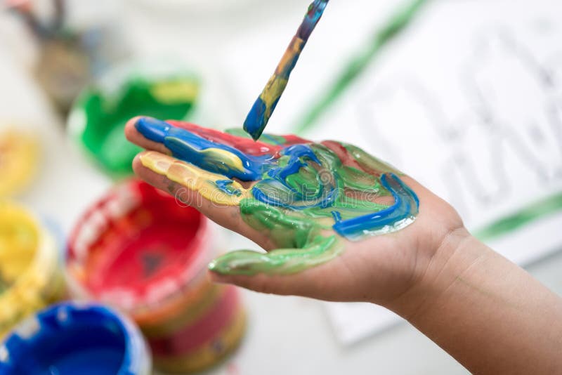 Child painting its hand with a paintbrush with colorful paint