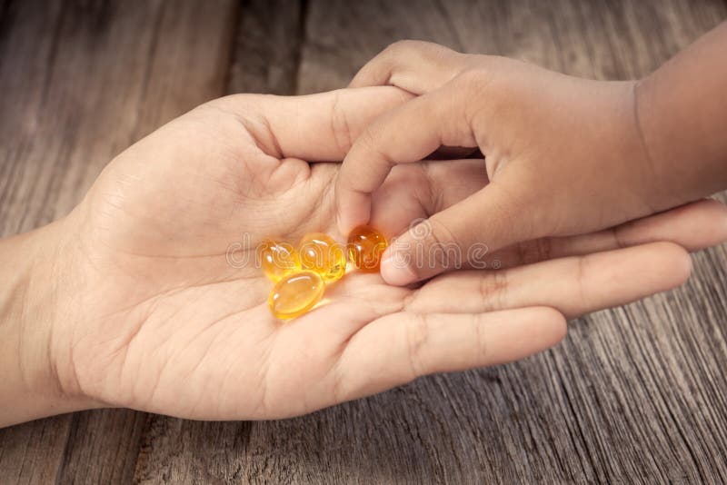 Child picks Cod liver oil omega 3 gel capsules on her mother hand