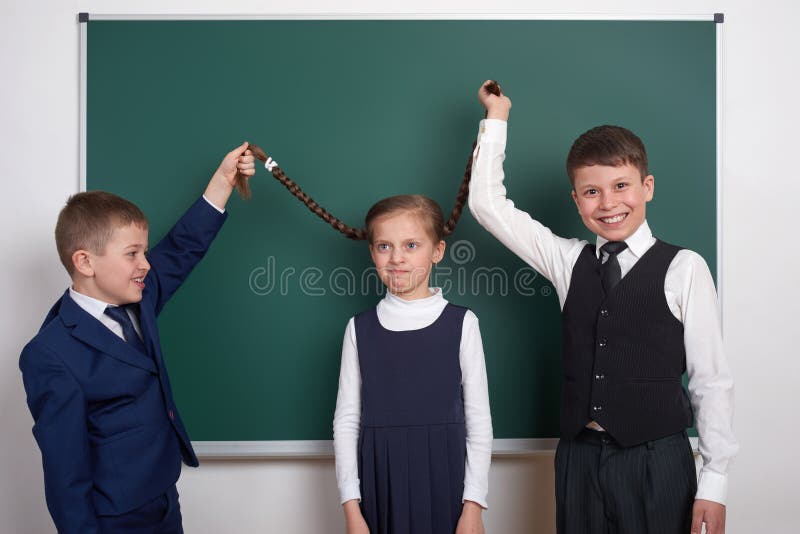 Child play and having fun, boys pull the girl braids, near blank school chalkboard background, dressed in classic black suit, grou