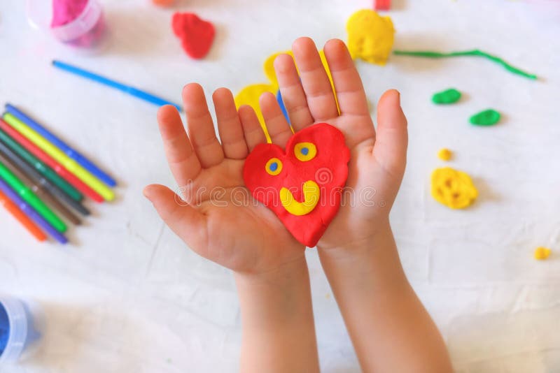 Child playing with plasticine, colorful modeling clay and sculpting heart . Home Education game with clay. Early development .