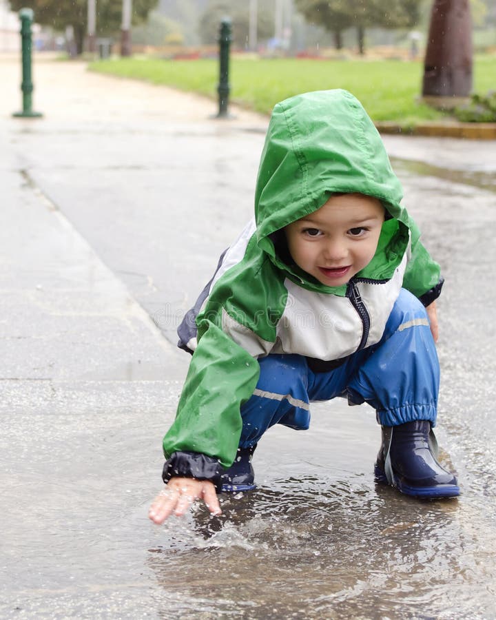 Child playing and splashing water in a puddle,. Child playing and splashing water in a puddle,