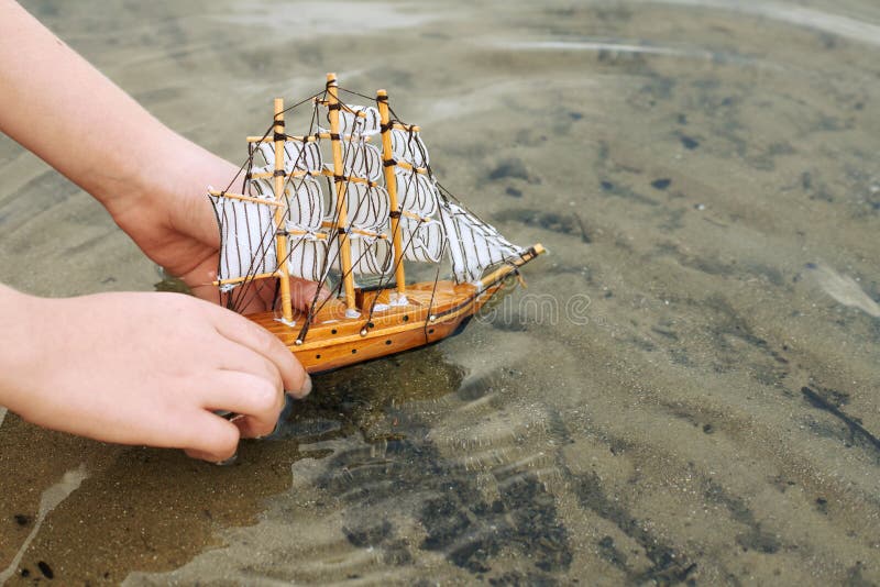 Child playing with a toy sailing ship by the river, hand closeup