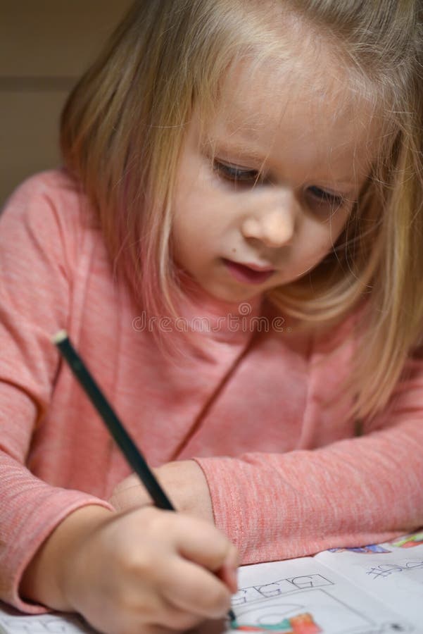 Child preschooler girl learns to draw and write in notebooks at home in the evening under the light from a desk lamp.