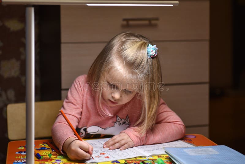 Child preschooler learns to draw and write in notebooks at home in the evening under the light from a desk lamp. House, beautiful.