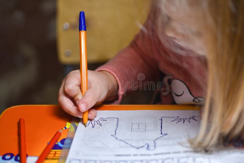 Child preschooler learns to draw and write in notebooks at home in the evening under the light from a desk lamp.