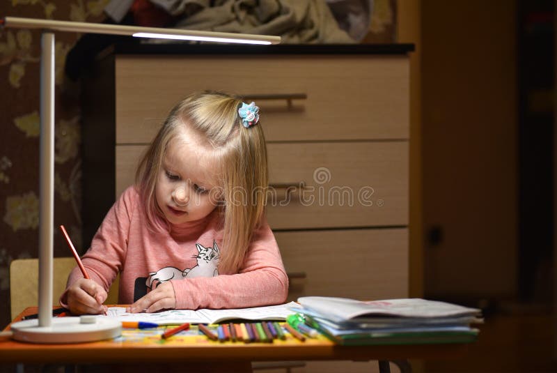 Child Preschooler Learns To Draw And Write In Notebooks At Home In The Evening Under The Light From A Desk Lamp.