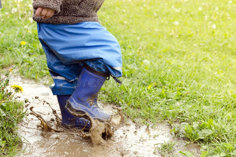 Child in boots jumping in muddy puddle after rain. Child in boots jumping in muddy puddle after rain.