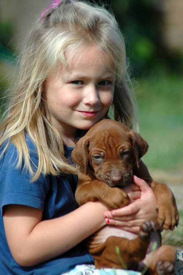 Krásne malý kaukazských biele dievča dieťa s dlhými blond vlasmi a radi s úsmevom výraz v jej krásna tvár, sedí spolu s jej roztomilý Rr kopov psa šteňa pet a objímať ho v záhrade na slnku vo vonkajšom prostredí.