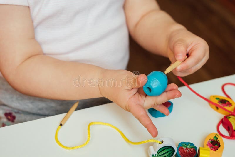 Child putting beads on a string. Bead stringing activity. Fine motor skills development