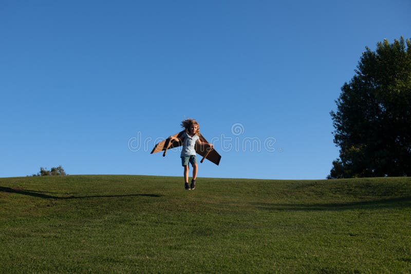 Child running jumping and flying with toy plane wings on grass in park. Child imagination dream to be pilot. Creative stock images