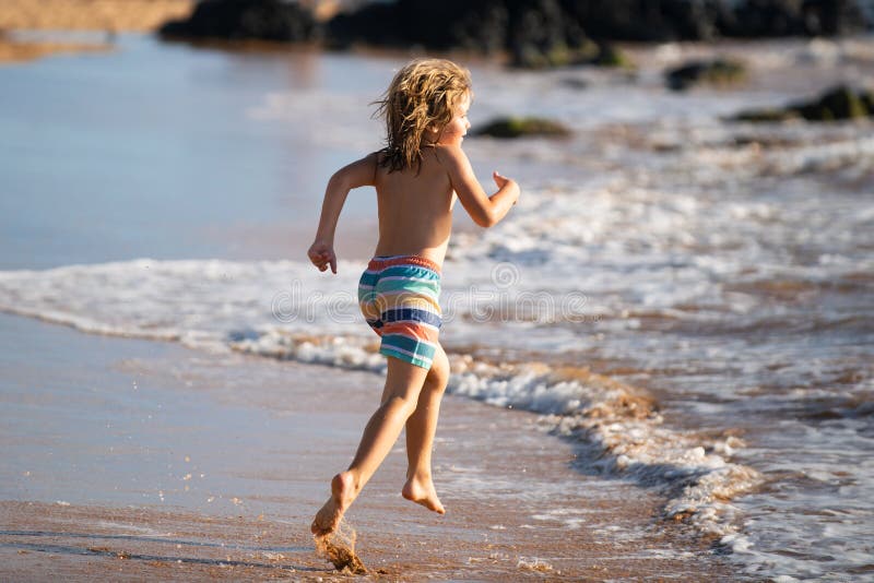 Child running through water close to shore along the sea beach. A boy runs along the sea coast. Rest of children on stock photos