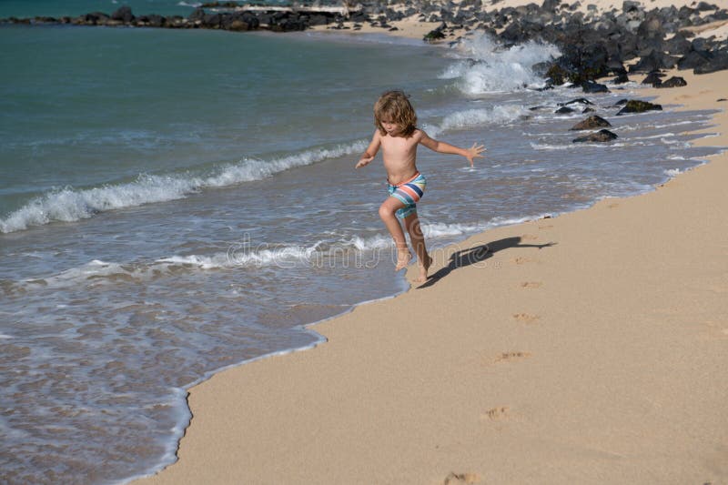 Child running through water close to shore along the sea beach. A boy runs along the sea coast. Rest of children on stock photos