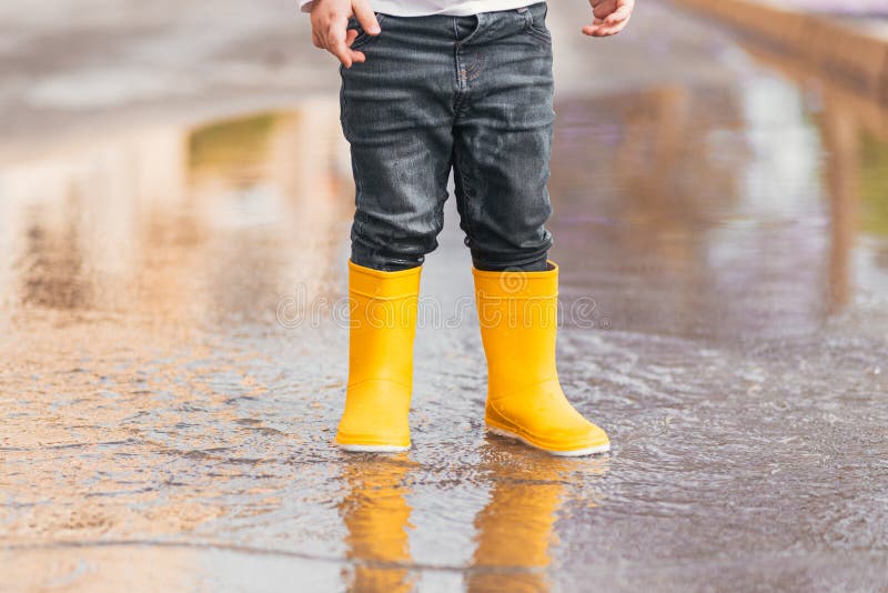 Child& X27;s Feet in Yellow Rubber Boots Jumping Over a Puddle in the ...