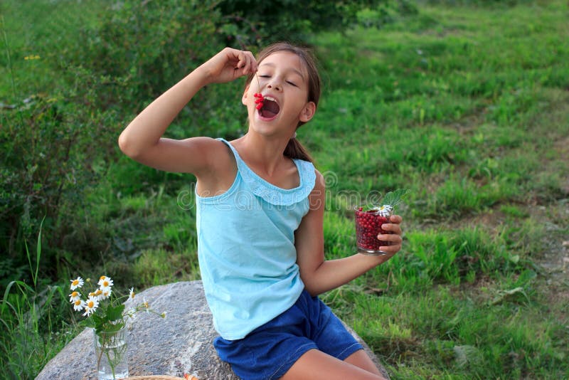 Child`s hand holding glass full of red currants in summer outdoors in garden