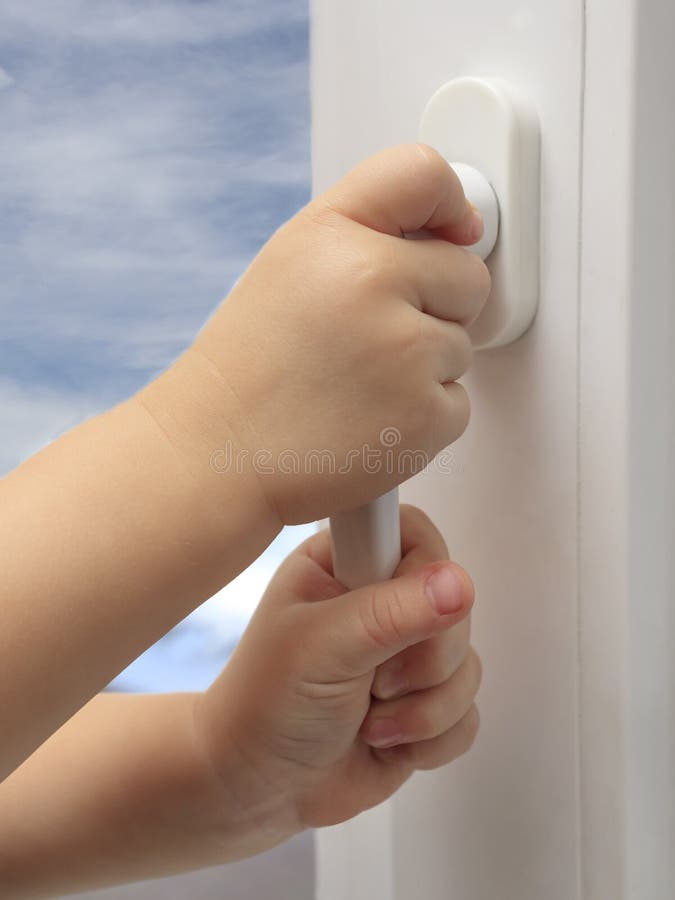 The child`s hands are holding the plastic window handle. The concept of children falling out of windows in multi-storey buildings, children`s safety. Cable safety guard prevent opening window by child.