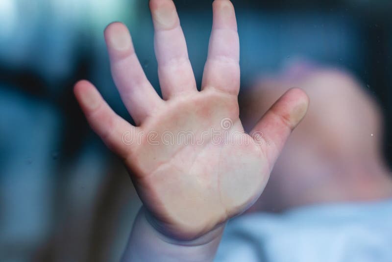 Child`s small hand is pressed against the window glass with reflection...