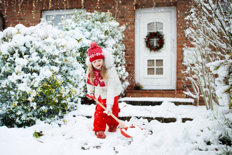 Child shoveling snow. Little girl with spade clearing driveway after winter snowstorm. Kids clear path to house door after