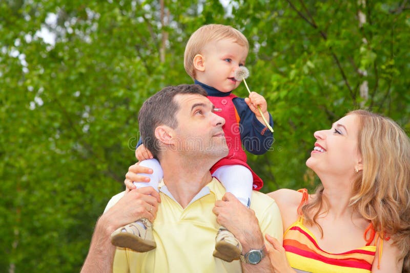 Child sits on shoulders of father with dandelion