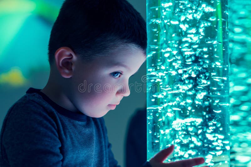 Child in therapy sensory stimulating room, snoezelen. Child interacting with colored lights bubble tube lamp during therapy.