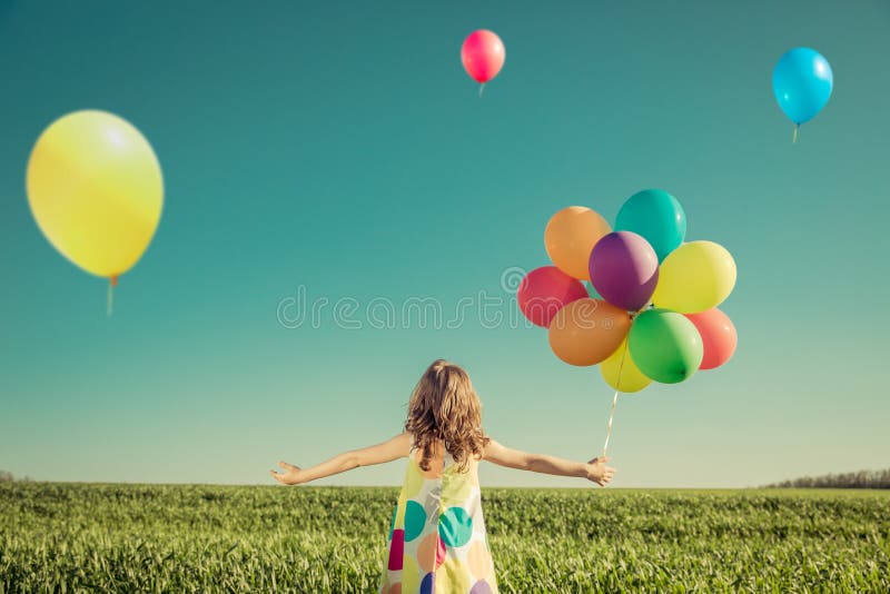 Child with toy balloons in spring field