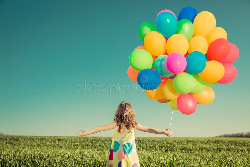 Child with toy balloons in spring field