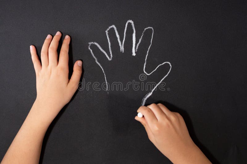 a child traces a hand with chalk on a black surface, DIY Halloween craft, tutorial step 1