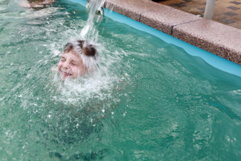 Child under stream of water in pool stock photography