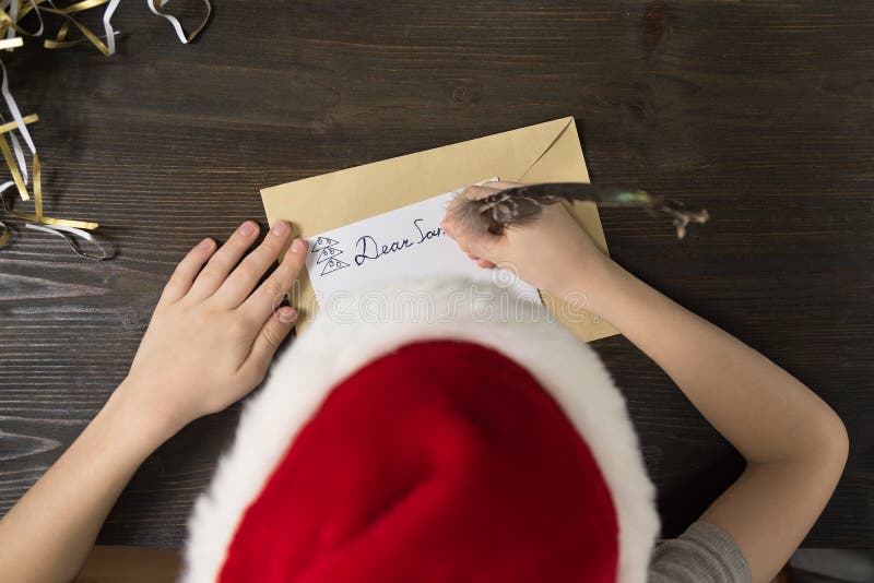 Child writes letter to Santa in santa`s hat. Top view. Christmas concept stock photo Child writes letter to Santa in santa`s hat. Top view. Christmas concept stock photo