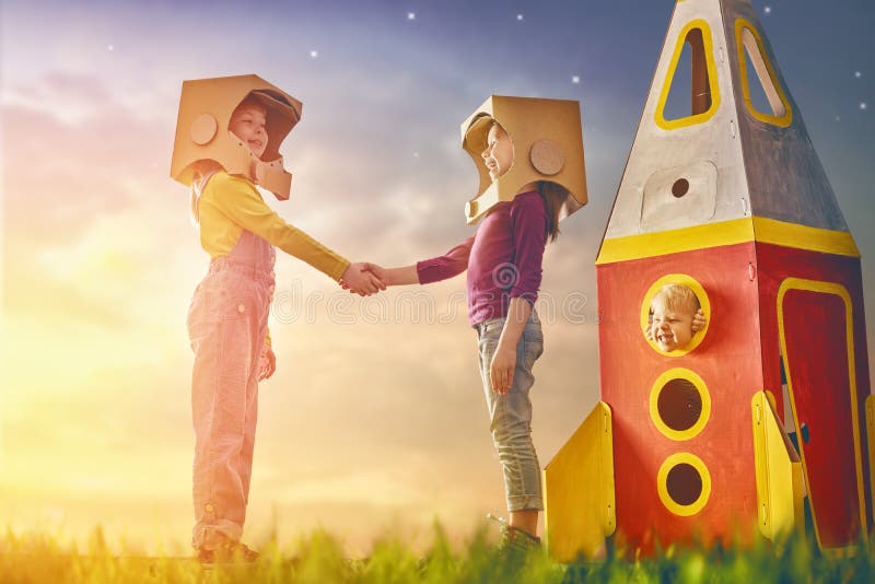 Children in astronauts costumes with toy rocket playing and dreaming of becoming a spacemen. Portrait of funny kids on a background of sunset star sky on nature. Family friends games outdoors.
