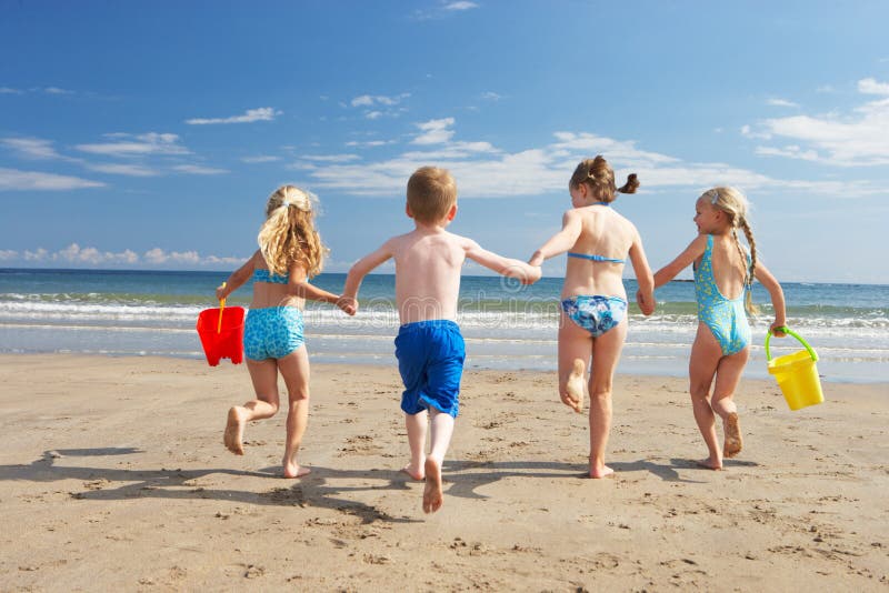 Děti na dovolenou na pláži běží směrem k oceánu.