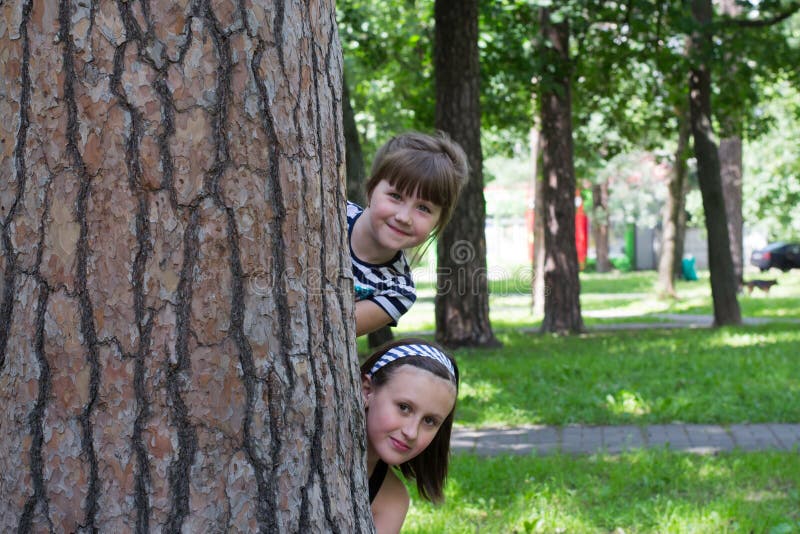 Funny kids in the park peeking from behind a tree. Funny kids in the park peeking from behind a tree