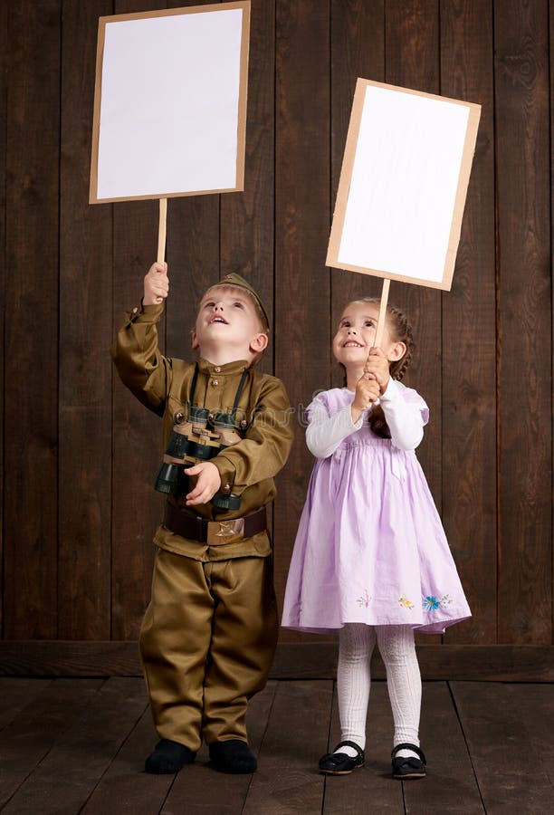 Children boy are dressed as soldier in retro military uniforms and girl in pink dress. They`re holding blank posters for veterans stock images Children boy are dressed as soldier in retro military uniforms and girl in pink dress. They`re holding blank posters for veterans stock images