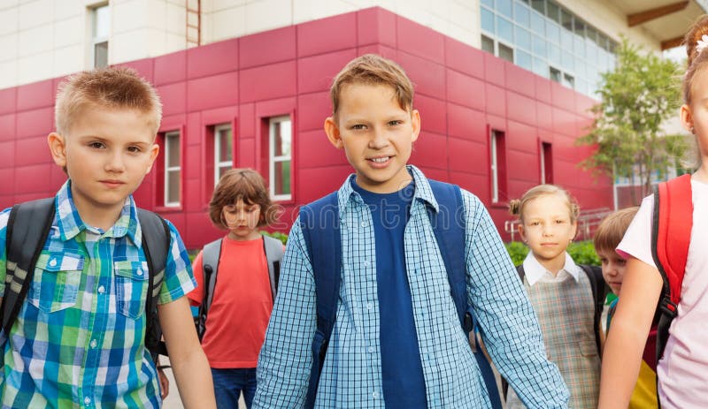 Children carry rucksacks and walk near school