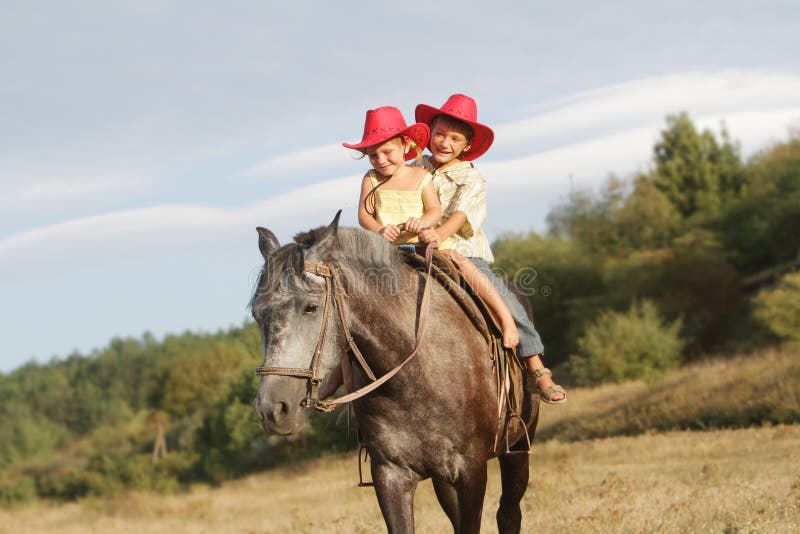 Children in cowboy hat riding horse outdoors
