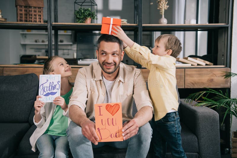 Children with fathers day gifts having fun with father holding greeting card with i love you dad inscription and heart