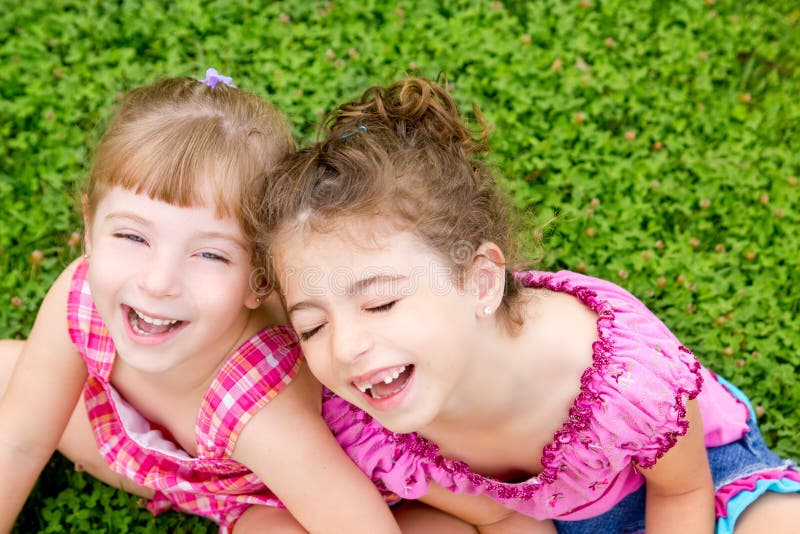 Deti, dievčatá smeje sedí na zelenej tráve v parku.