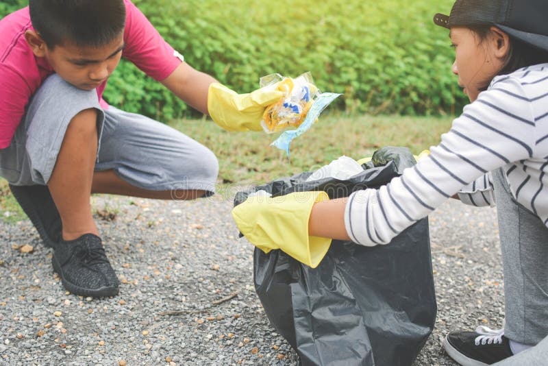 Children hand in yellow gloves picking up empty of bottle plastic into bin bag