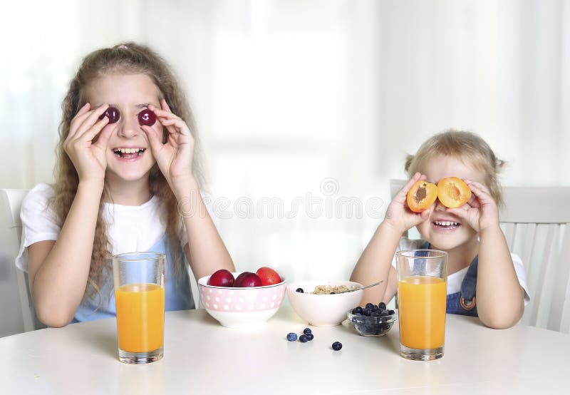 Children have fun,girls eating fruits.Two sisters sitting at table have a meal