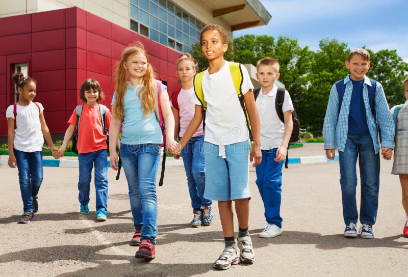 Children holding hands carry rucksacks and walk