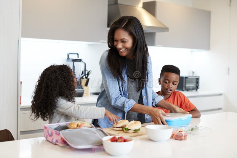 Children In Kitchen At Home Helping Mother To Make Healthy Packed Lunch