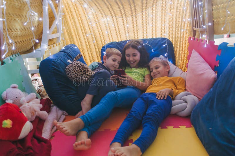 Children play with smartphone at home lying on pillows under the covered blanket royalty free stock photos