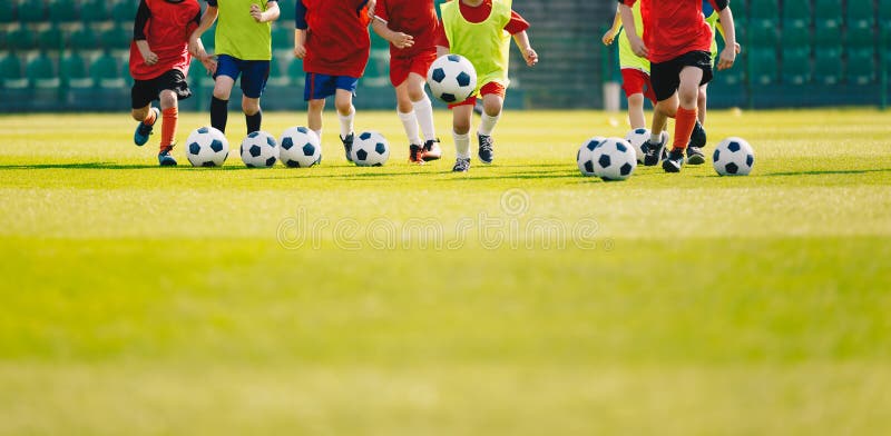 Children play soccer at grass sports field. Football training for kids. Children running and kicking soccer balls at soccer pitch. Soccer background with copy space on the bottom