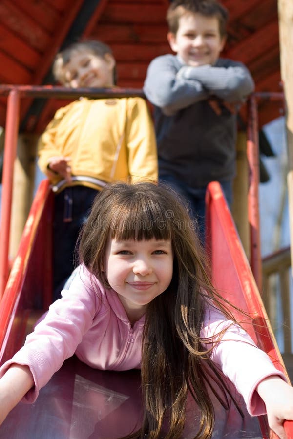 Smiling girl is sliding headfirst down a playground sliding board, while her two smiling brothers are standing at the top of the sliding board. Focus is on the little girl. Top smiling cheerful stock images, royalty-free photos and pictures