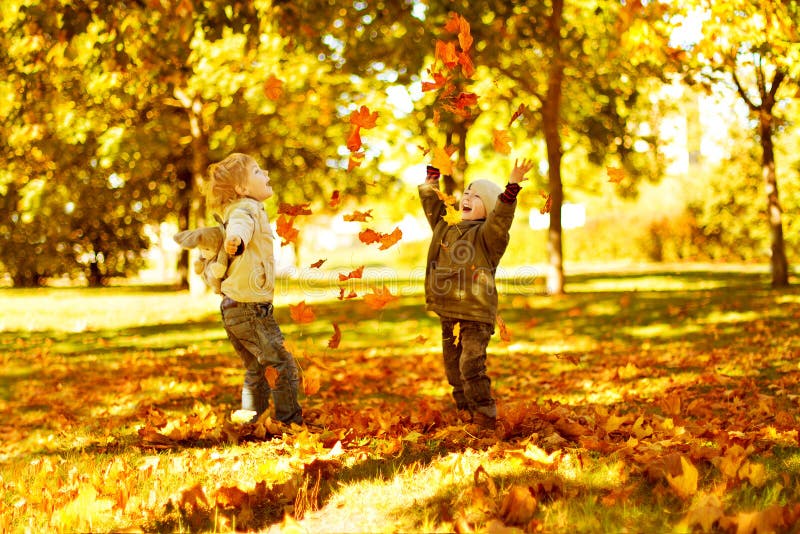 Children playing with autumn fallen leaves in maple park